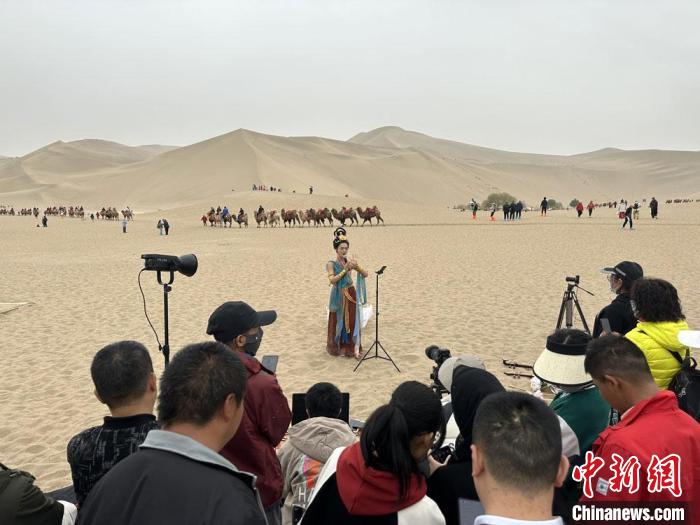 圖為2023年4月底，敦煌大漠“逐舞者”奧楠在鳴沙山月牙泉景區(qū)視頻直播，吸引游人圍觀?！●T志軍 攝